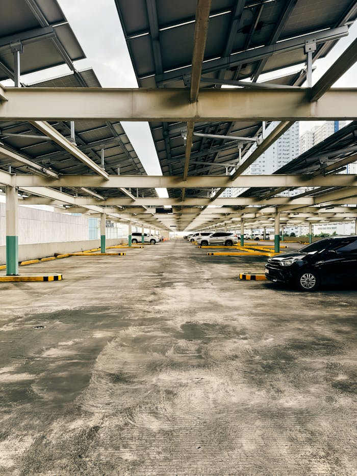 Covered parking lot with solar panels and cars in an urban setting, daylight view.
